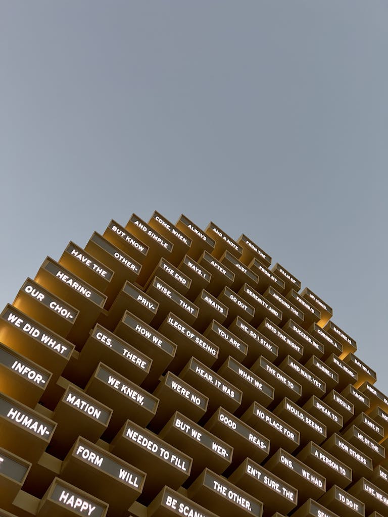 Abstract modern sculpture featuring illuminated text panels against a clear sky.